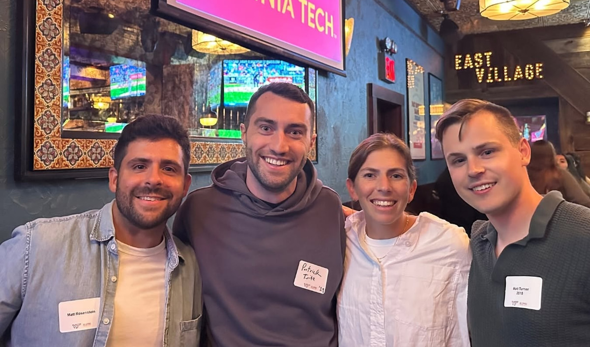 Four people gathered beneath a Virginia Tech screen at a New York venue