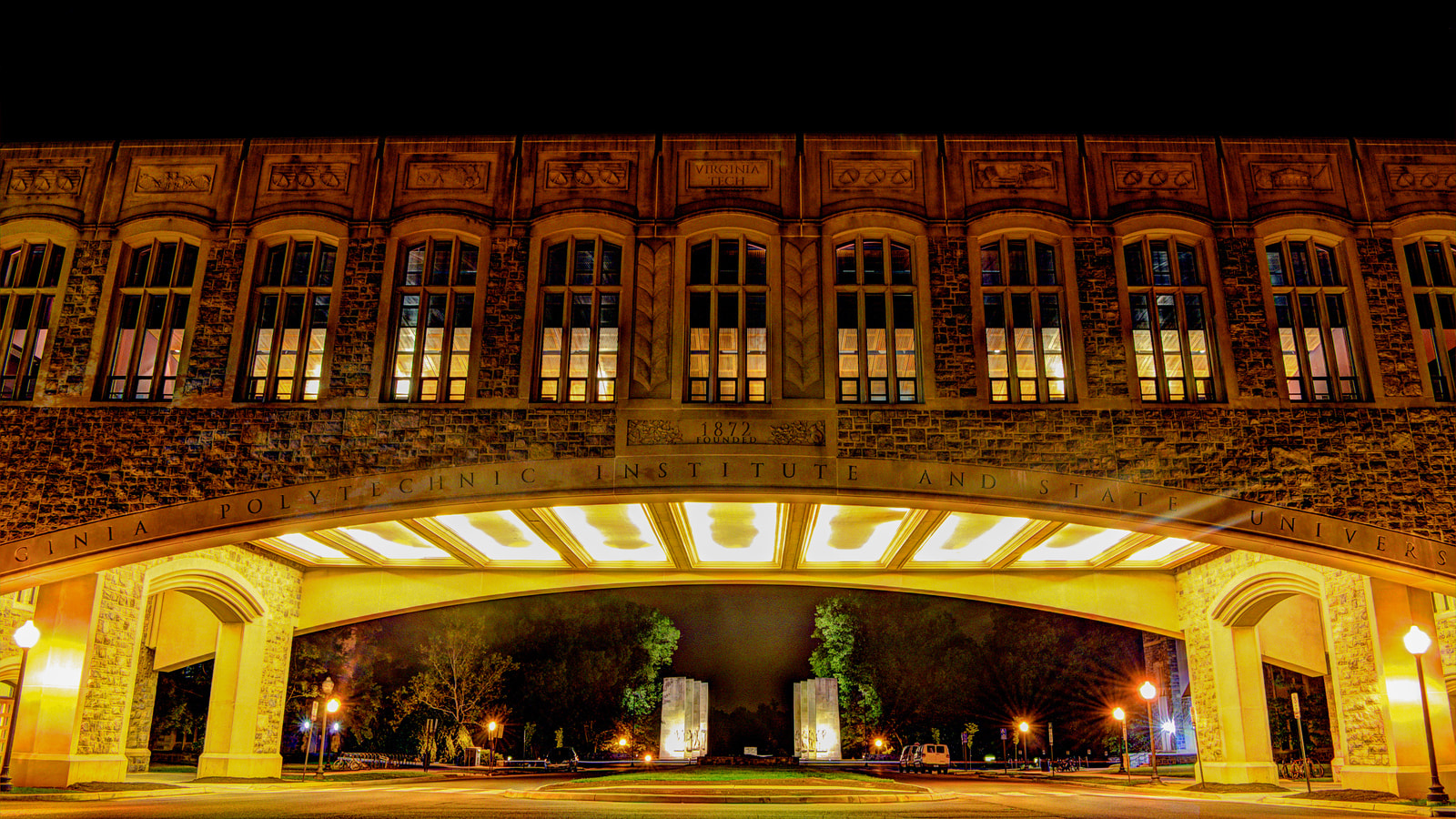 A Virginia Tech campus arch and stone building illuminated at night
